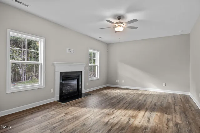 a view of an empty room with wooden floor fireplace and a window