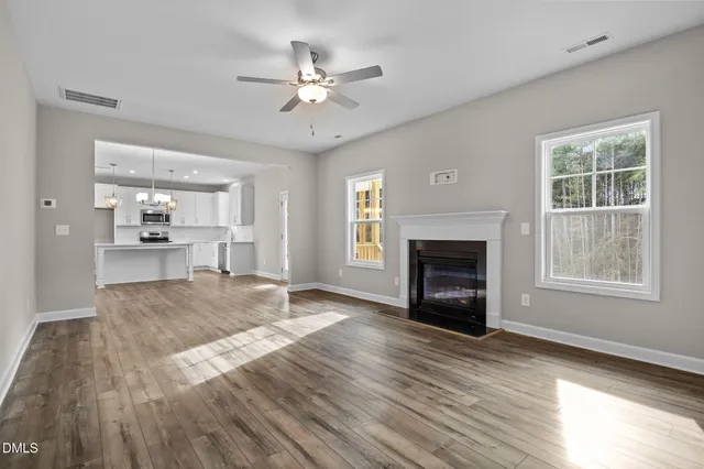 a view of an empty room with wooden floor fireplace and a window
