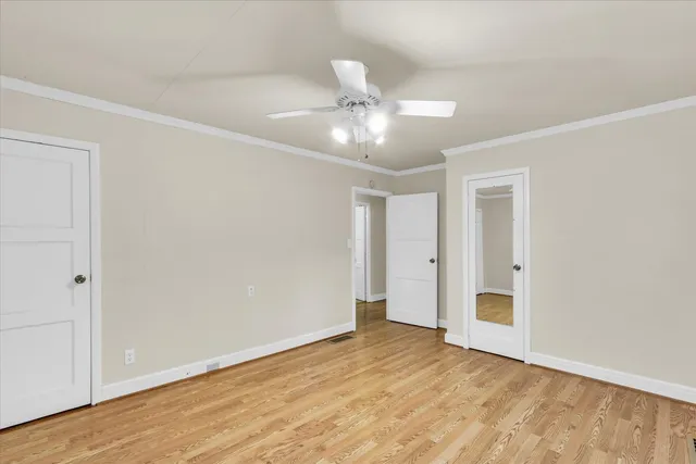 a view of an empty room with wooden floor and a ceiling fan