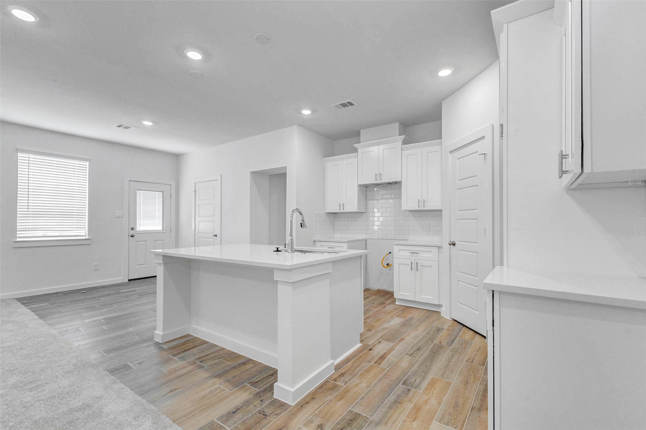 6471 Escondido Drive Rosharon, TX 77583 - Photo 15 of 33 Bright kitchen view featuring a large center island, white cabinetry, quartz-style countertops, subway tile backsplash, recessed lighting, and wood-look tile flooring. The open layout connects easily to the dining and living areas, creating a clean, functional space for meal prep, casual seating, and entertaining.