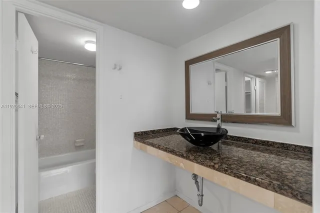 a bathroom with a granite countertop sink and mirror with bathtub