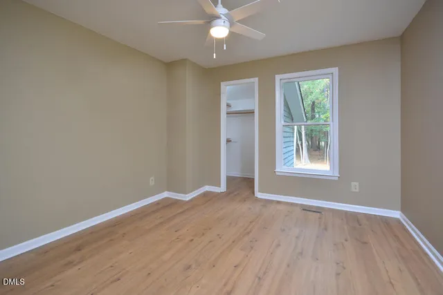 an empty room with wooden floor ceiling fan and windows