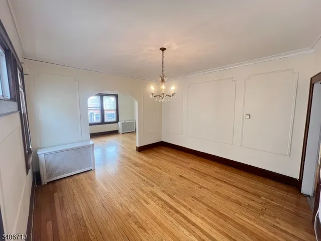 an empty room with wooden floor chandelier and windows
