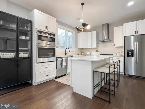 a kitchen with stainless steel appliances kitchen island granite countertop a stove a refrigerator and white cabinets with wooden floors