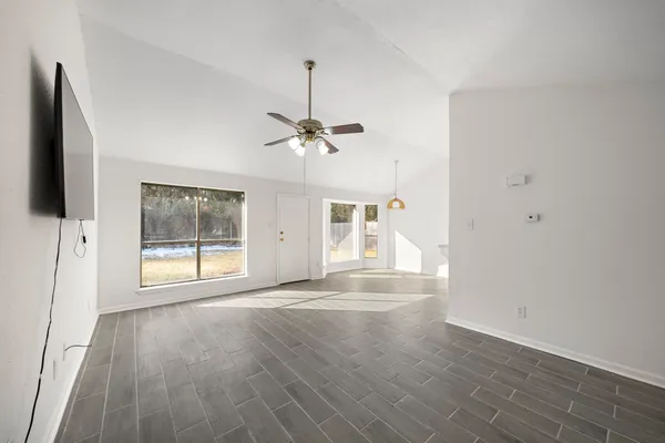 an empty room with wooden floor fan and windows