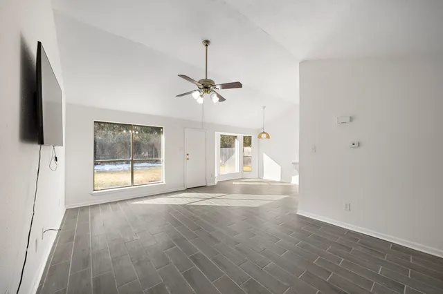 an empty room with wooden floor fan and windows