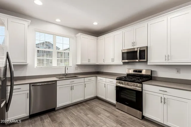 a kitchen with stainless steel appliances granite countertop white cabinets a sink a stove a microwave and wooden floors