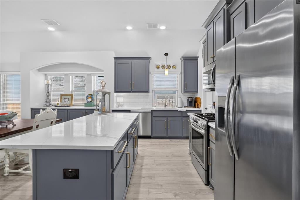 833 Godley Ranch Godley, TX 76044 - Photo 11 of 31 Kitchen featuring a large center island with a white countertop and dark gray cabinetry, stainless steel appliances, white subway tile backsplash, and wood-finish flooring