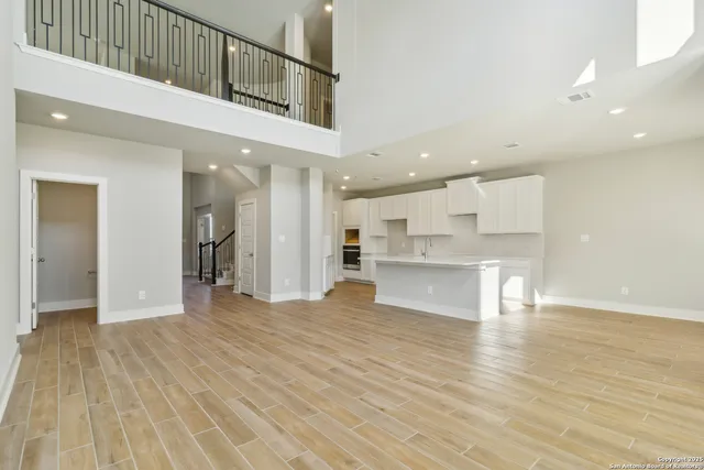 a view of an empty room and kitchen view with wooden floor