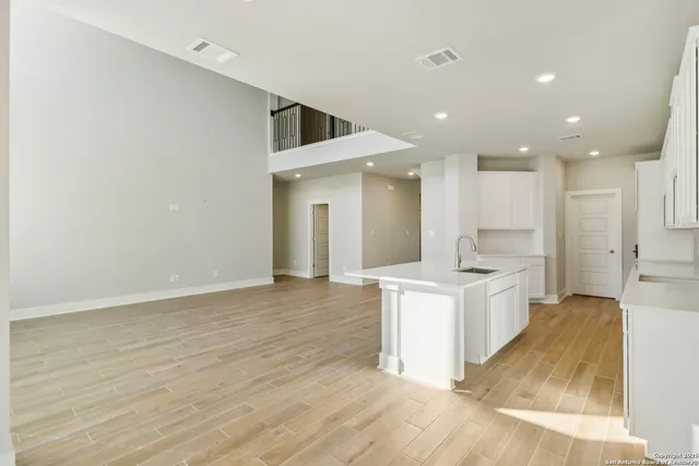 a large white kitchen with kitchen island a sink wooden floor and a refrigerator