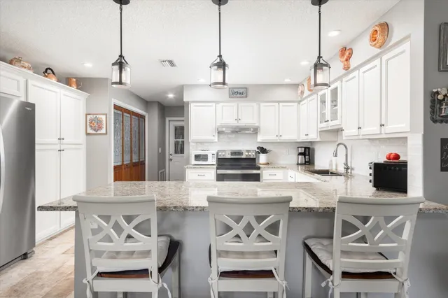 a kitchen with stainless steel appliances granite countertop a stove top oven a refrigerator a sink and chairs