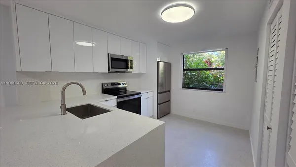 a kitchen with stainless steel appliances granite countertop a sink a stove a refrigerator a window with white cabinets and a wooden floor