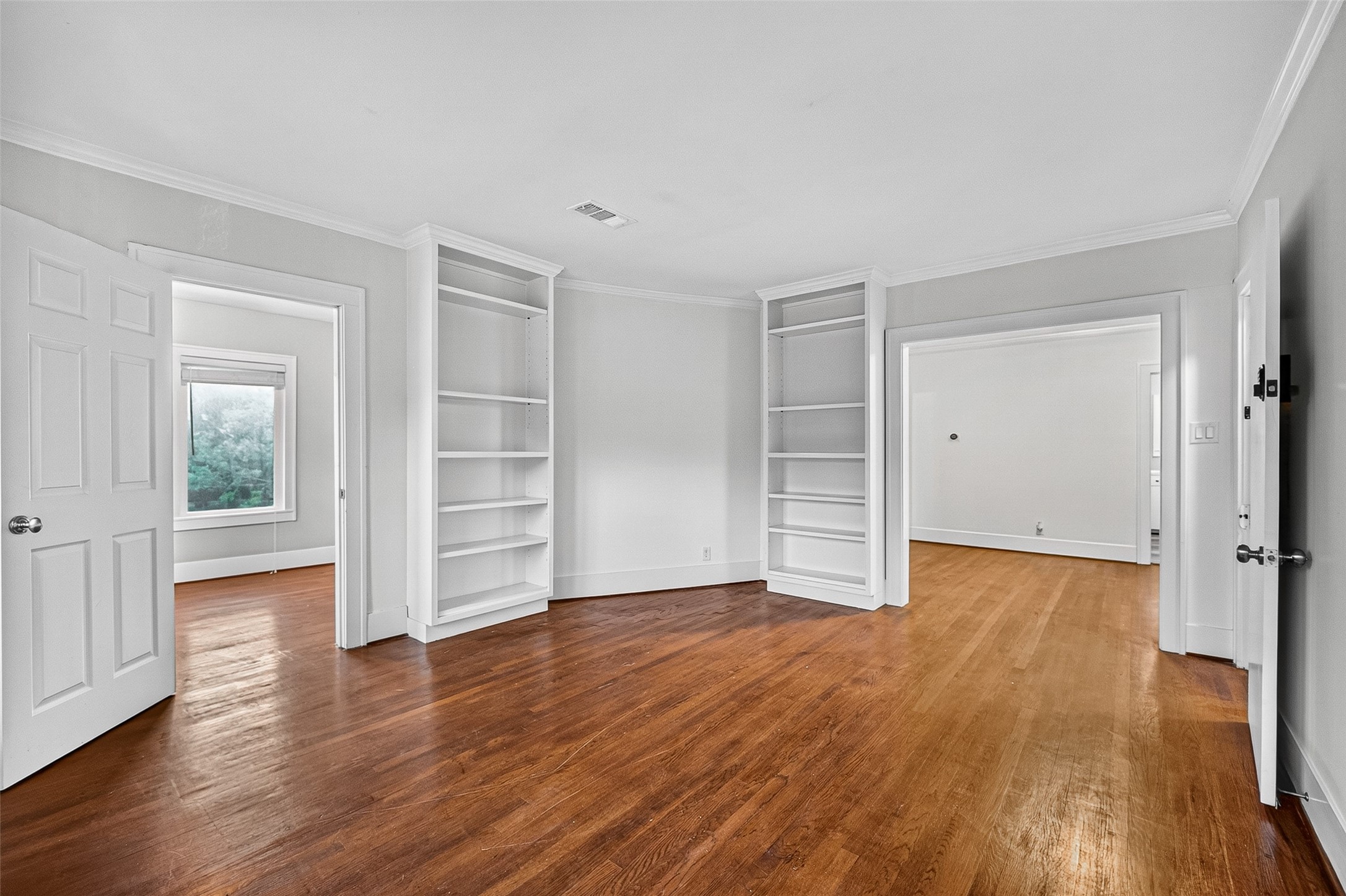 1758 Hawthorne Street, Unit 2 Houston, TX 77098 - Photo 3 of 19 This photo showcases a spacious living area with polished hardwood floors and neutral gray walls. It features crown molding and multiple doorways leading to adjacent rooms, creating an open and airy flow. Large windows in a nearby room allow natural light to brighten the space.