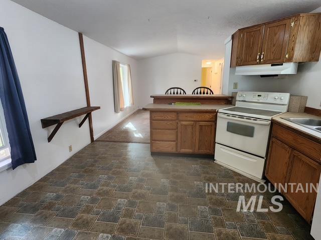 1220 North 4th Street Parma, ID 83660 - Photo 11 of 23 Kitchen featuring electric stove, stone finish floors, a peninsula, vaulted ceiling, and brown cabinets