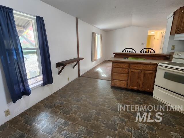 1220 North 4th Street Parma, ID 83660 - Photo 10 of 23 Kitchen featuring stone finish flooring, white range with electric stovetop, a peninsula, brown cabinetry, and healthy amount of natural light