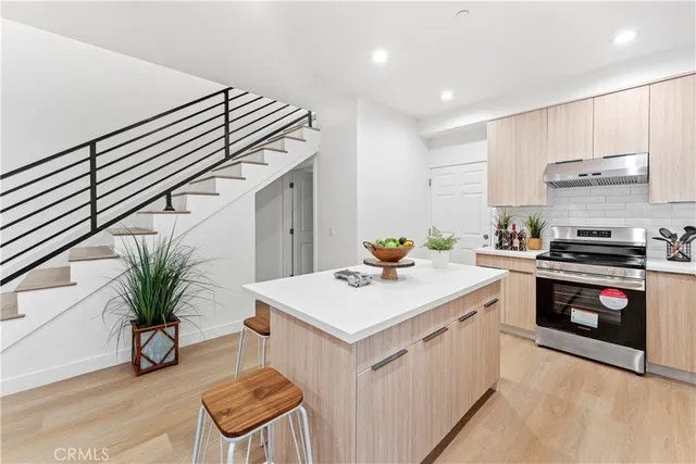 a kitchen with kitchen island a sink a stove a refrigerator and white cabinets with wooden floor