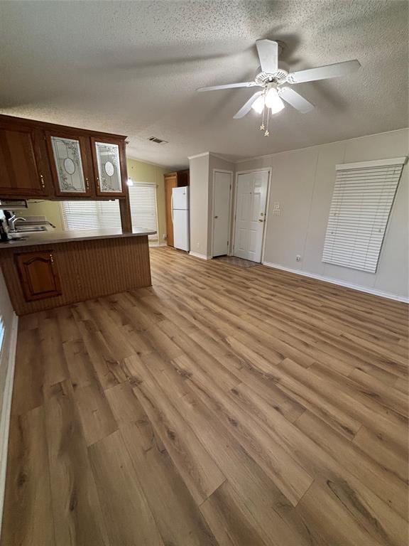 206 Holiday Rambler Drive Whitney, TX 76692 - Photo 16 of 28 Open-concept living area featuring wood-finish flooring, a ceiling fan with integrated lighting, and a kitchen bar with wood cabinetry and decorative glass inserts
