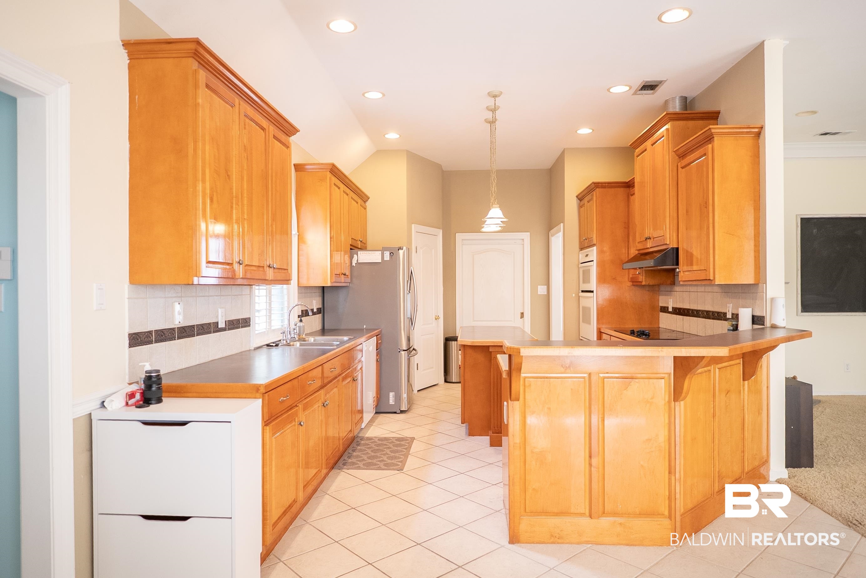 10023 Springfield Court Mobile, AL 36695 - Photo 16 of 50 Kitchen with decorative backsplash, a peninsula, a breakfast bar, hanging light fixtures, and light tile patterned flooring