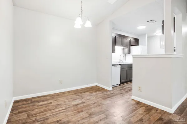 an empty room with wooden floor and kitchen view