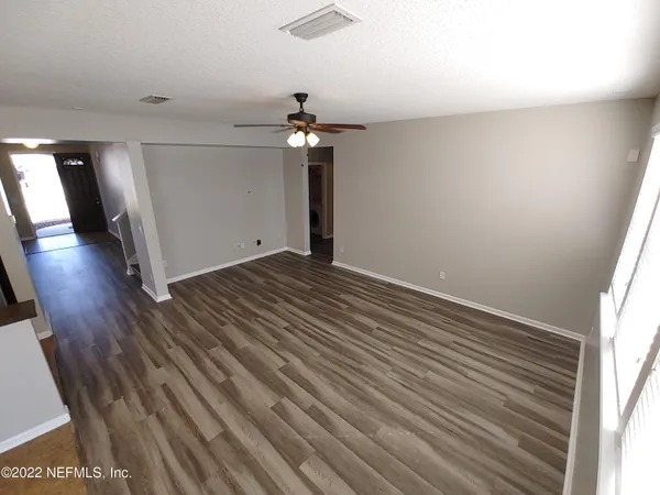 an empty room with wooden floor chandelier fan and windows