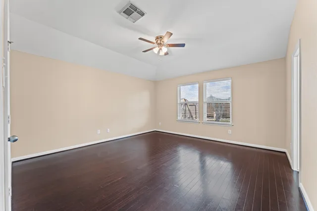 an empty room with wooden floor fan and windows