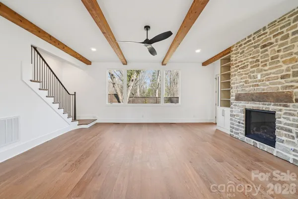 a view of an empty room with wooden floor fireplace and a window