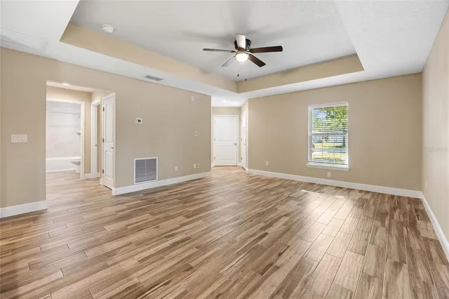 a view of an empty room with wooden floor ceiling fan