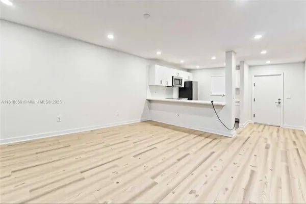 a view of empty room with wooden floor and kitchen