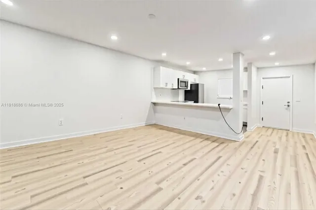 a view of empty room with wooden floor and kitchen