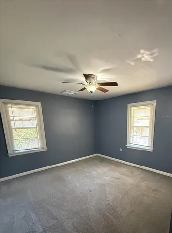 an empty room with windows and ceiling fan