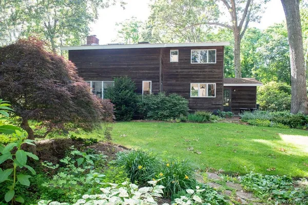 a view of a brick house with a small yard plants and large trees