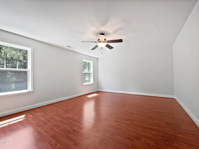 an empty room with wooden floor chandelier fan and windows
