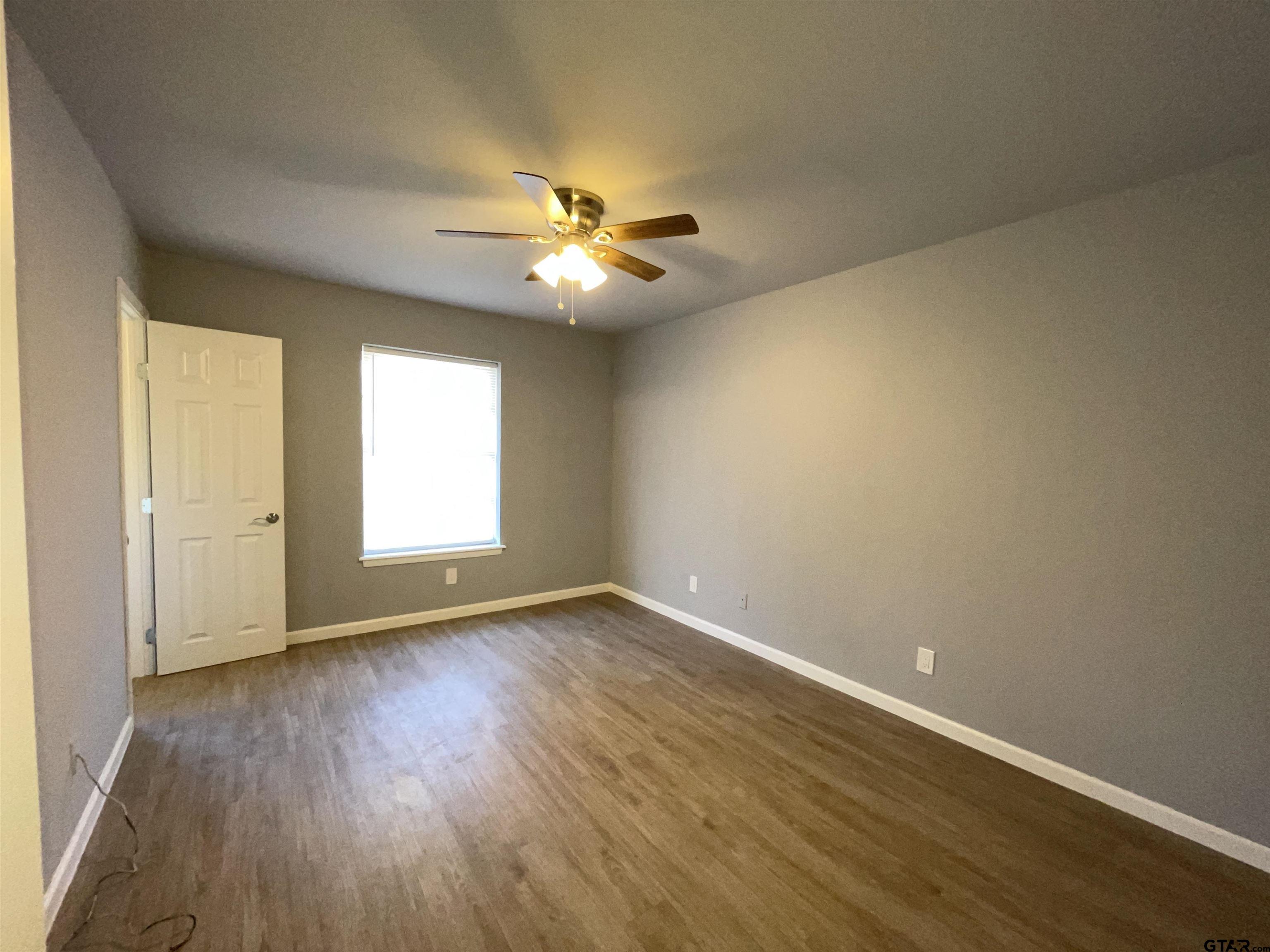 625 Augusta Avenue, Unit 10 Tyler, TX 75701 - Photo 7 of 9 an empty room with wooden floor chandelier fan and windows