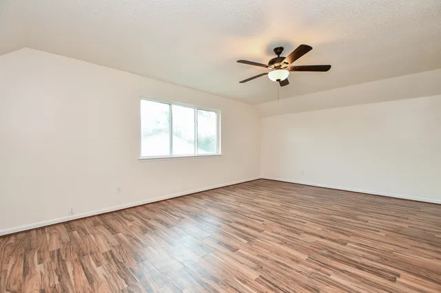 an empty room with wooden floor fan and windows