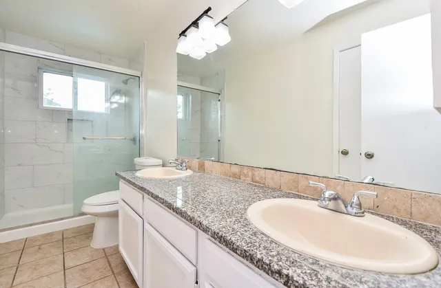 a bathroom with a granite countertop sink a toilet a mirror and shower