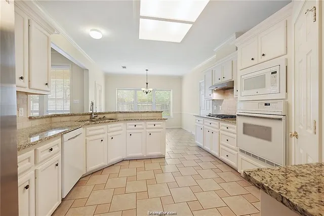 a large white kitchen with granite countertop a stove a sink dishwasher and a refrigerator