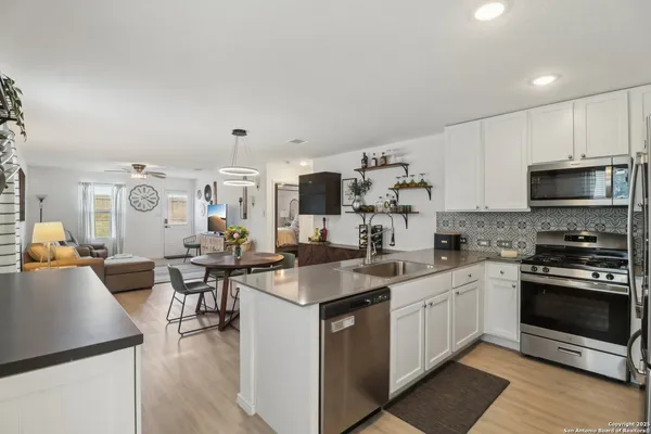 a open kitchen with stainless steel appliances granite countertop a stove top oven a sink dishwasher and white cabinets with wooden floor