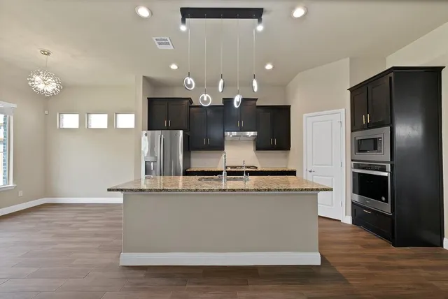 a large kitchen with stainless steel appliances kitchen island a large counter top and wooden floor