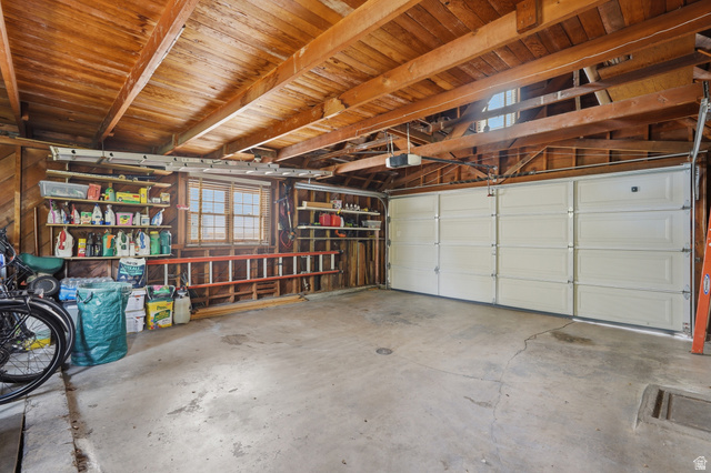 7576 South Jefferson Street Midvale, UT 84047 - Photo 44 of 53 Concrete-floored garage featuring a white panel garage door, exposed wood beam ceiling, wood-paneled walls, and built-in shelving