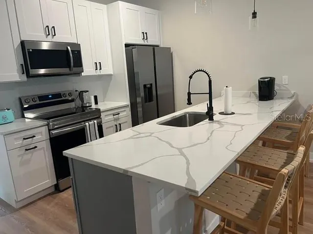 a kitchen with stainless steel appliances kitchen island granite countertop a refrigerator a stove a sink and white cabinets