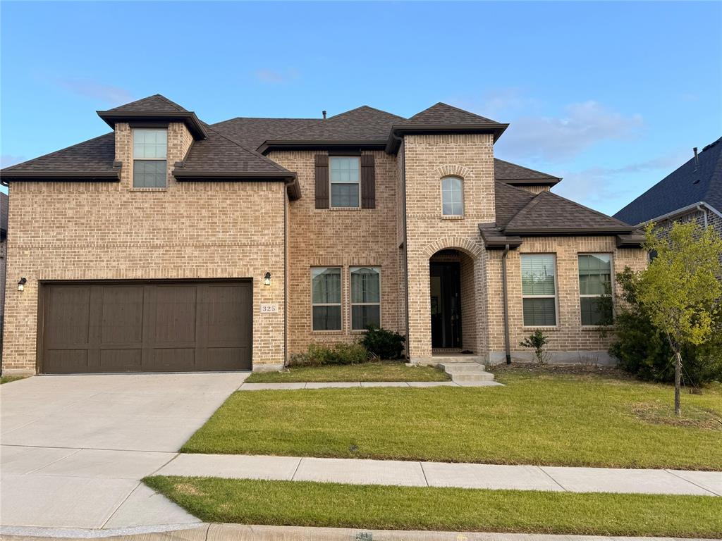French country home featuring a front yard, brick siding, concrete driveway, roof with shingles, and a garage