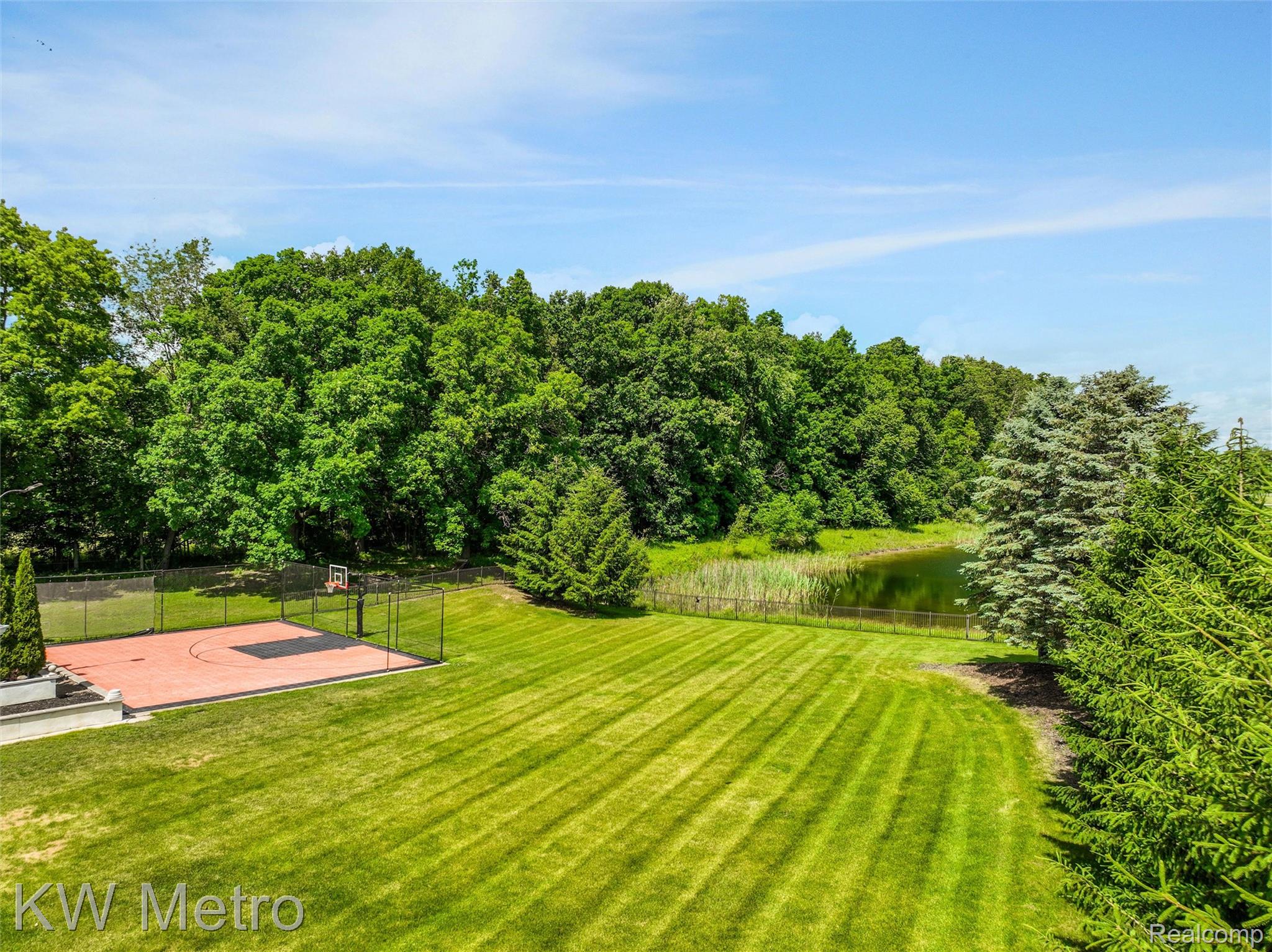 65884 Windrose Court Ray, MI 48096 - Photo 12 of 82 Expansive manicured lawn featuring a fenced sport court, mature trees, and a pond with natural landscaping