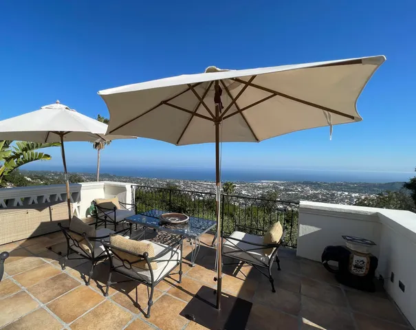 a view of a patio with couches table and chairs under an umbrella with a fireplace