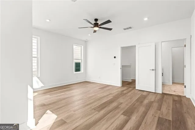 an empty room with wooden floor ceiling fan and windows
