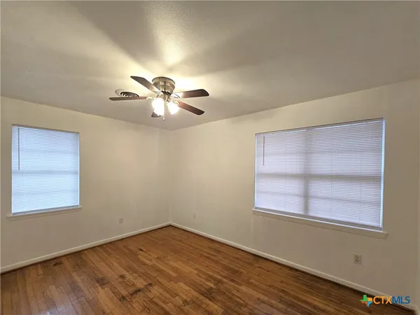 an empty room with wooden floor chandelier fan and windows