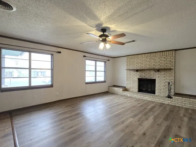 an empty room with windows fireplace and a kitchen view