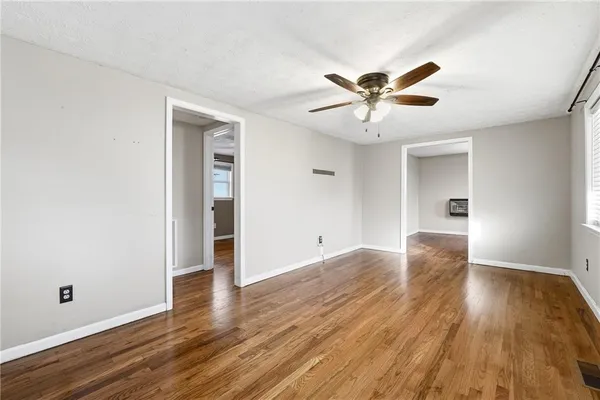 an empty room with wooden floor chandelier fan and windows