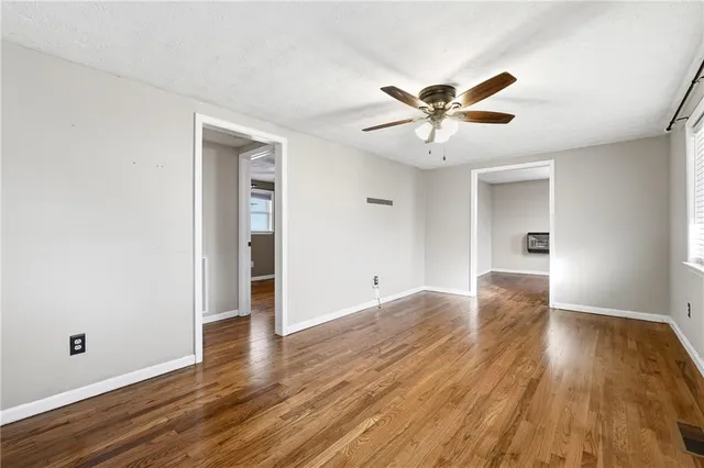 an empty room with wooden floor chandelier fan and windows