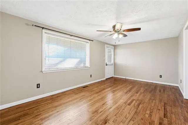 an empty room with wooden floor ceiling fan and windows