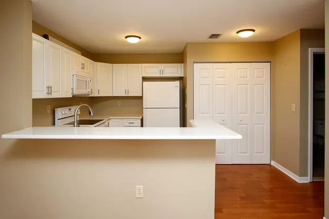 a kitchen with stainless steel appliances a refrigerator a sink dishwasher and white cabinets with wooden floor